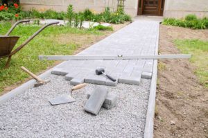 Bricklayer places concrete paving stone blocks for building up a patio, using hammer and spirit level crushed concrete for pathway